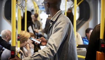 En man med en mobiltelefon i handen som står upp i en buss.