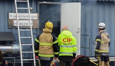 Räddningstjänstpersonal och CIP utanför en rökfylld byggnad.