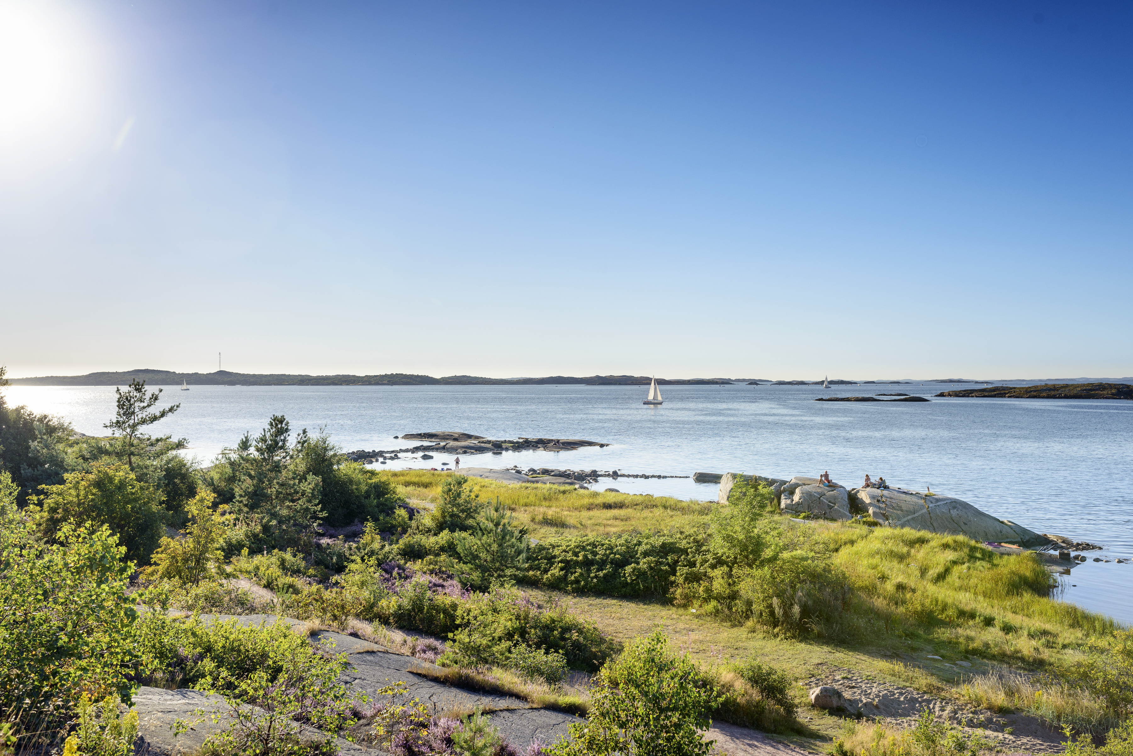 Vy över västkusten med hav, klippor, båtar och badande.