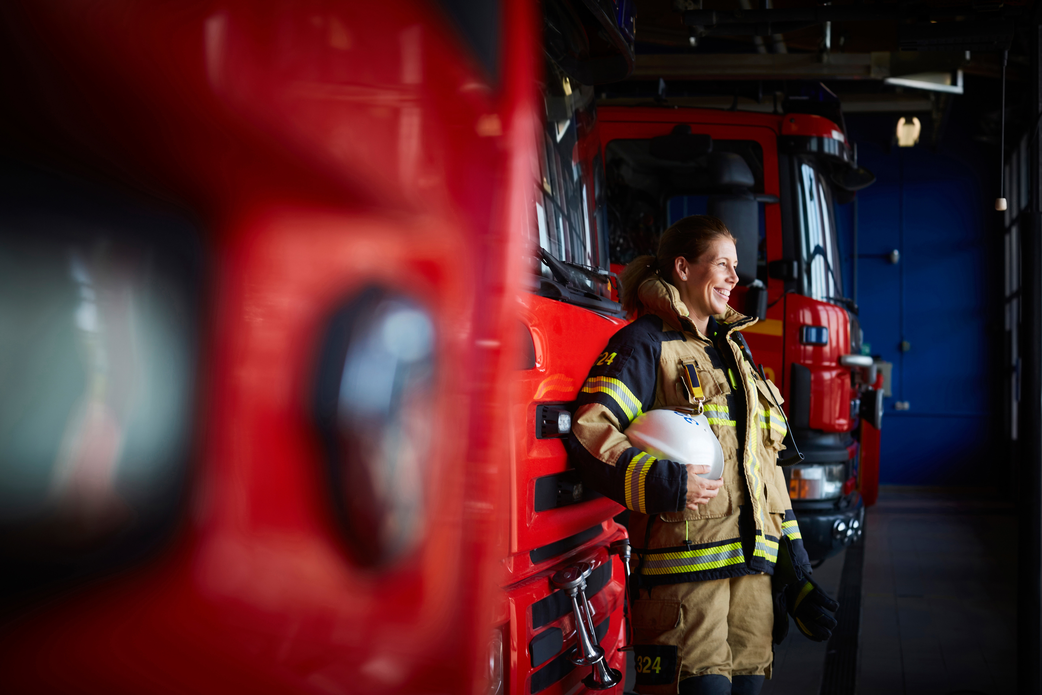 Kvinna som ler ståendes framför en brandbil på en brandstation.