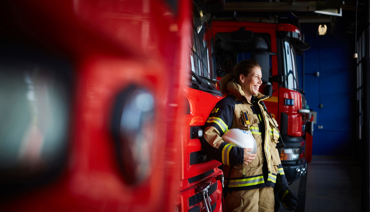 Kvinna som ler ståendes framför en brandbil på en brandstation.