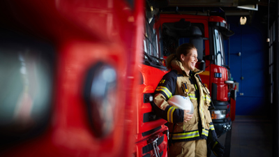Kvinna som ler ståendes framför en brandbil på en brandstation.