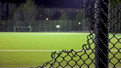 Trasigt stängsel framför ett fotbollsfält.
