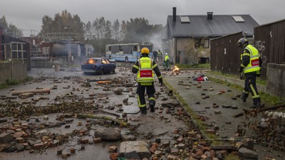 Räddningstjänstpersonal vid en övning där bränder syns i bakgrunden.